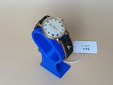 une montre posée sur un présentoir bleu, avec une étiquette de prix accrochée dessus