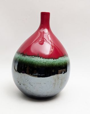 a red and green vase sitting on a white surface
