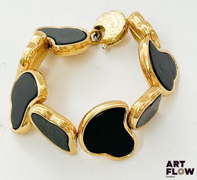 une image représentant un bracelet noir et doré posé sur une surface blanche