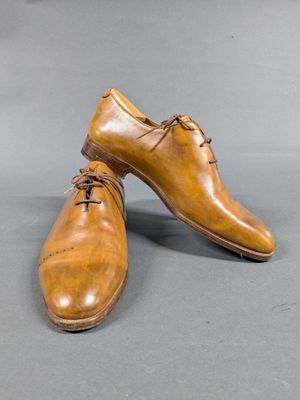 pair of brown leather shoes with laces on them on a gray surface