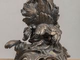 a silver statue of a bird on a leafy stand