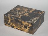 une image représentant une boîte en marbre noir et doré posée sur une surface blanche
