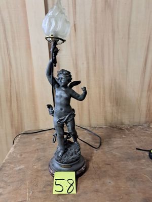 une petite statue représentant un garçon tenant une lampe, posée sur une table