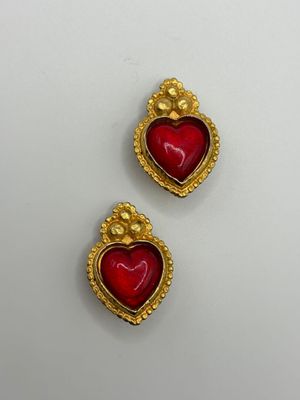 a pair of gold and red heart shaped earrings on a white surface