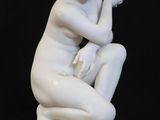 a white statue of a woman sitting on a black surface