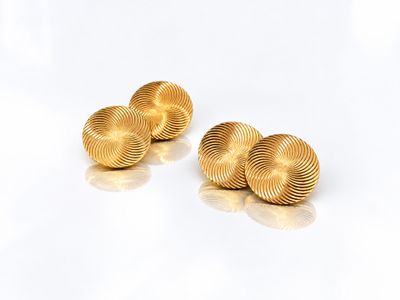une paire de boutons de manchette en or posés sur une surface blanche
