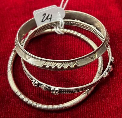 trois bracelets rigides en argent avec une étiquette, posés sur un tissu rouge