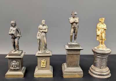 quatre statues en bronze représentant des hommes et des femmes, posées sur des socles disposés sur une table