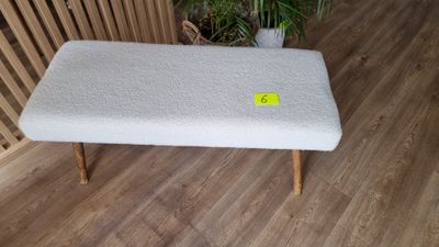 Petit banc en tissu blanc et piètement bois.
