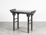 une table en bois noir avec un plateau en verre, posée sur un sol en béton