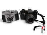 two cameras sitting next to each other on a white surface