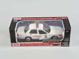 une voiture de police miniature dans une boîte, posée sur une surface blanche