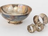 un bol en argent et deux bagues en argent posés sur une surface blanche