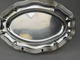 an antique silver plate with a scalloped edge on a gray surface