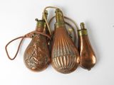 three antique brass bottles with handles and a rope on a white surface
