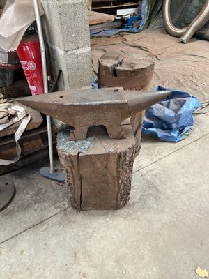 une vieille enclume posée sur une table, à côté d'un tas de vieux outils
