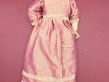 an old doll with a pink dress and black shoes on a red surface