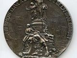 une vieille médaille surmontée d'une statuette, posée sur une surface blanche