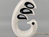 une lampe blanche surmontée d'un oiseau noir et blanc