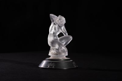 a crystal figurine of a woman sitting on a black surface