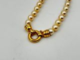 a pearl necklace with a gold clasp on a white surface