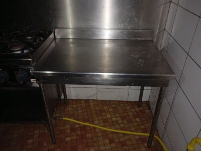 une table en acier inoxydable dans une cuisine, avec un tuyau jaune posé par terre
