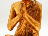 statue of a golden buddha sitting on the ground with his hands folded