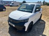 La petite voiture blanche est garée sur un parking, avec d'autres voitures en arrière-plan.
