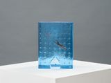 une petite sculpture en verre posée sur un socle blanc