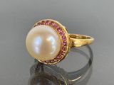 a close up of a ring with a pearl and pink stones