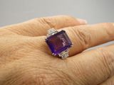 une image représentant la main d'une femme tenant une bague sertie d'une pierre violette et d'un diamant
