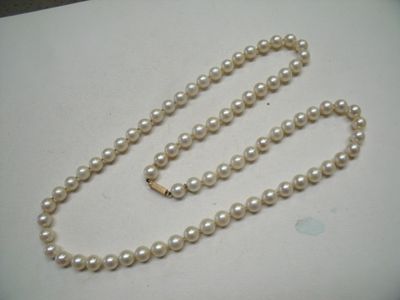 un collier de perles blanches muni d'un fermoir en or, posé sur une table