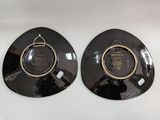 two black plates with gold trims are on a white surface