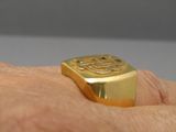 a man ' s hand holding a gold ring with a symbol on it