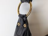 black leather handbag hanging on a white wall with a gold ring
