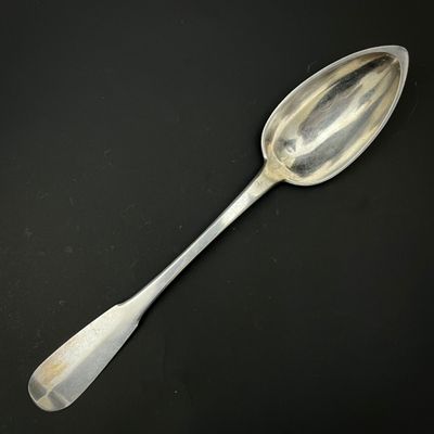 une vieille cuillère en argent à long manche posée sur une surface noire
