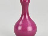 un vase violet posé sur une surface blanche, sur fond gris