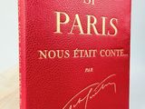 un livre rouge avec des lettres dorées posé sur une surface blanche