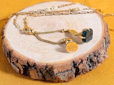 a necklace with a coin and a chain on a piece of wood
