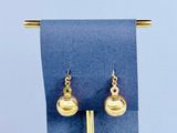 des boucles d'oreilles posées sur un présentoir recouvert d'un tissu bleu, surmonté d'une boule dorée