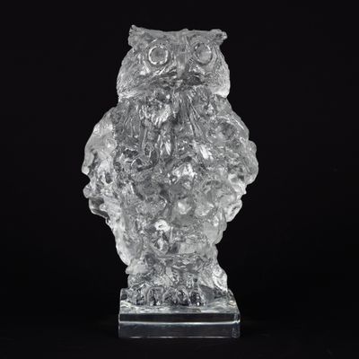 figurine de chouette en cristal posée sur un socle transparent, sur fond noir