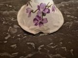 a white vase with purple flowers on it sitting on a table