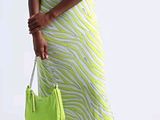une femme vêtue d'une robe jaune et blanche, tenant un sac à main vert
