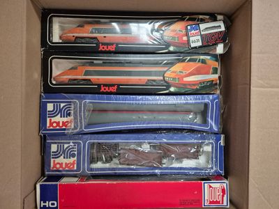 des boîtes contenant un assortiment de petits trains miniatures, rangées dans un carton posé sur une table