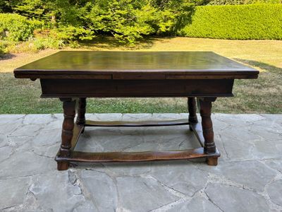 une table en bois sur une terrasse en pierre, avec un buisson en arrière-plan