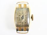 une montre en or avec un cadran blanc posée sur une surface blanche