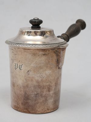 une vieille casserole en argent avec une poignée en bois posée sur une surface blanche