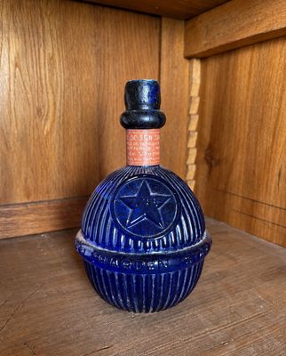 une bouteille en verre bleue ornée d'un pentagramme, posée sur une étagère en bois
