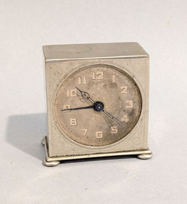une petite horloge argentée posée sur une surface blanche