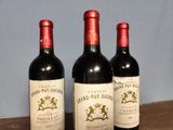 three bottles of red wine sit on a table in front of a blue wall